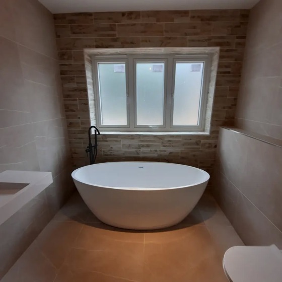 Freestanding bath under a window, with the window wall tiled as a feature in a brick effect tile