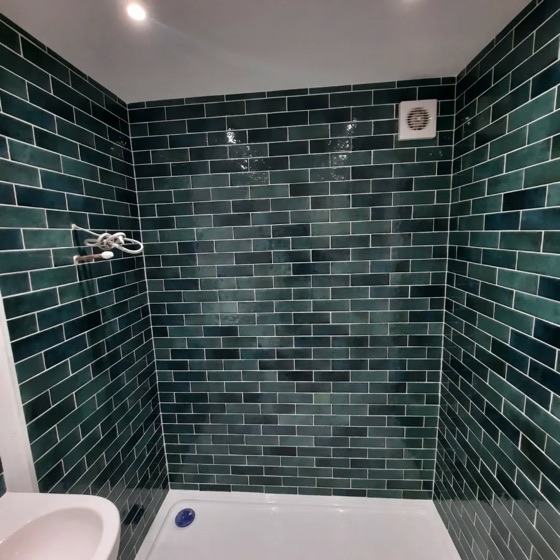 Deep green subway tile laid brick bond in a small shower area