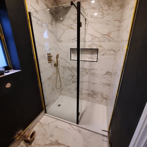 Marble effect gloss wall tile in a shower, with a black framed screen and brass shower fittings