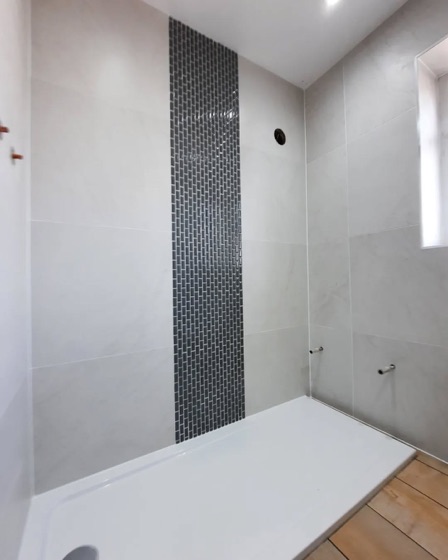 Off white square tile with a vertical mosaic border running down the wall